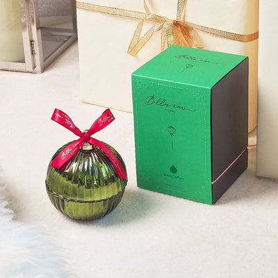 green bauble with red ribbon on a white floor and behind it a white gift box with some gold ribbon, green packaging