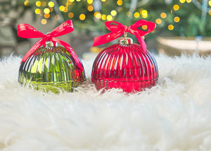 green scented bauble and red scented bauble, on a fluffy white rug, with yellow guirlande light and christmas tree